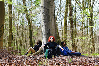 In a spring forest, people from different backgrounds are sitting around a large tree, leaning against it, resting with their eyes closed.